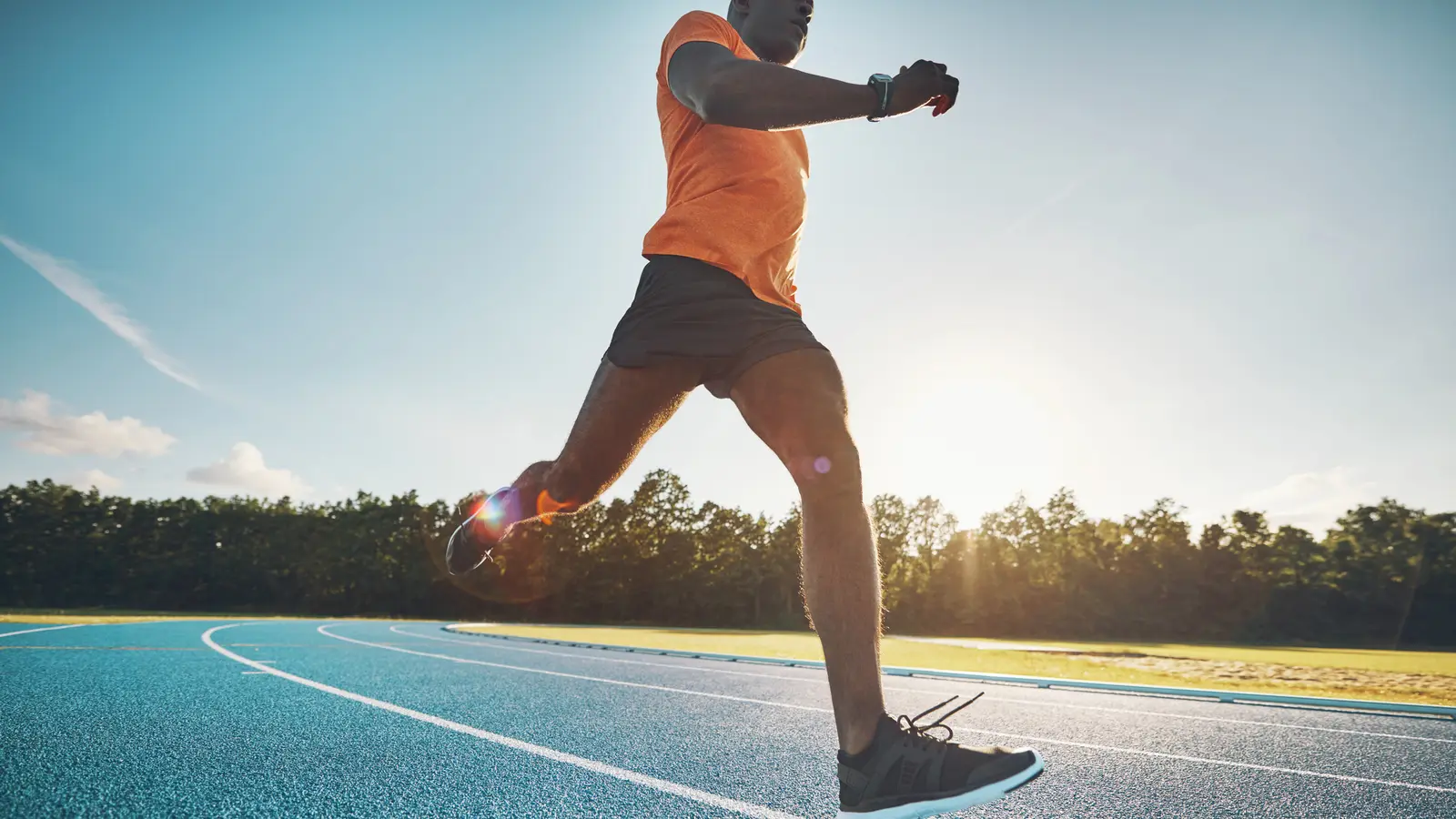 Sporcu güneşli bir günde atletizm pistinde hızlı koşuyor
